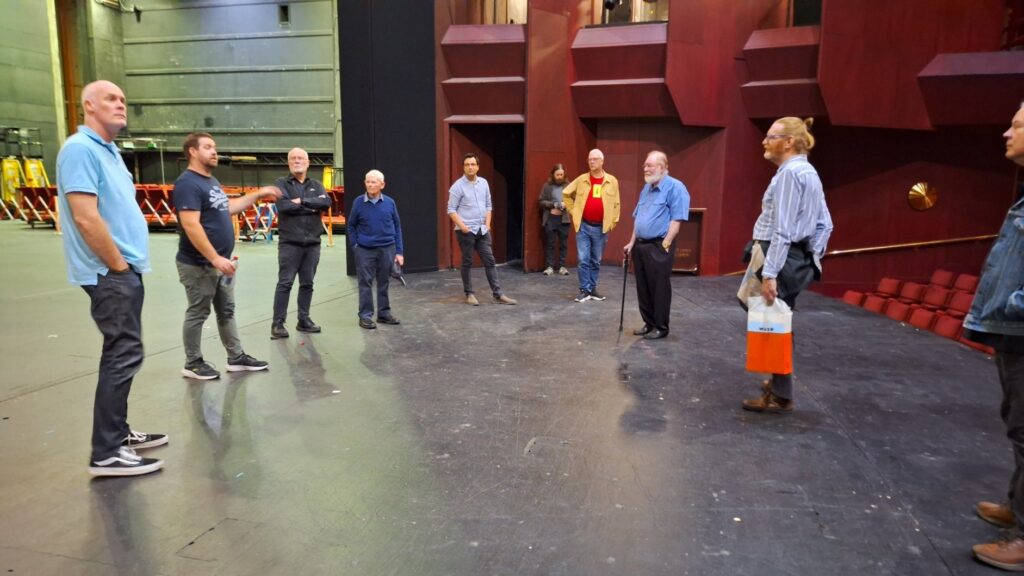 Image shows Nick Walker talking to a group of the visitors, explaining the orchestra pit operations