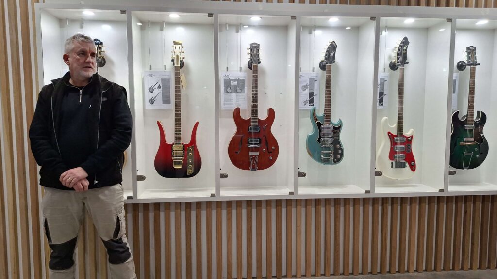 Patrick Evans, in the reception area of Maton Guitars, stands in front of a selection of Maton Guitars displayed behind glass