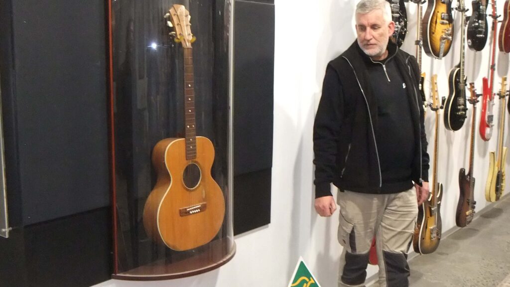 Patrick Evans stands next to a Maton Guitar behind glass from the original 1946 production run.